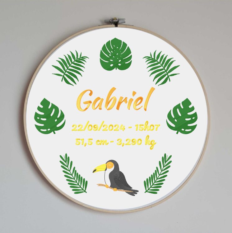 Cercle en bois avec un tissu en coton blanc brodé avec des motifs de jungle et un toucan ainsi que toutes les informations de naissance de bébé : prénom, date, heure, taille et poids de naissance