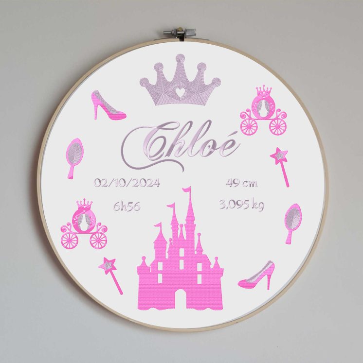 Cercle en bois avec un tissu blanc brodé avec toutes les informations de naissance de bébé et des motifs sur le thème des princesses et avec un château